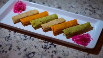 A white rectangular plate with six rolled items in various colors, placed on a granite countertop.