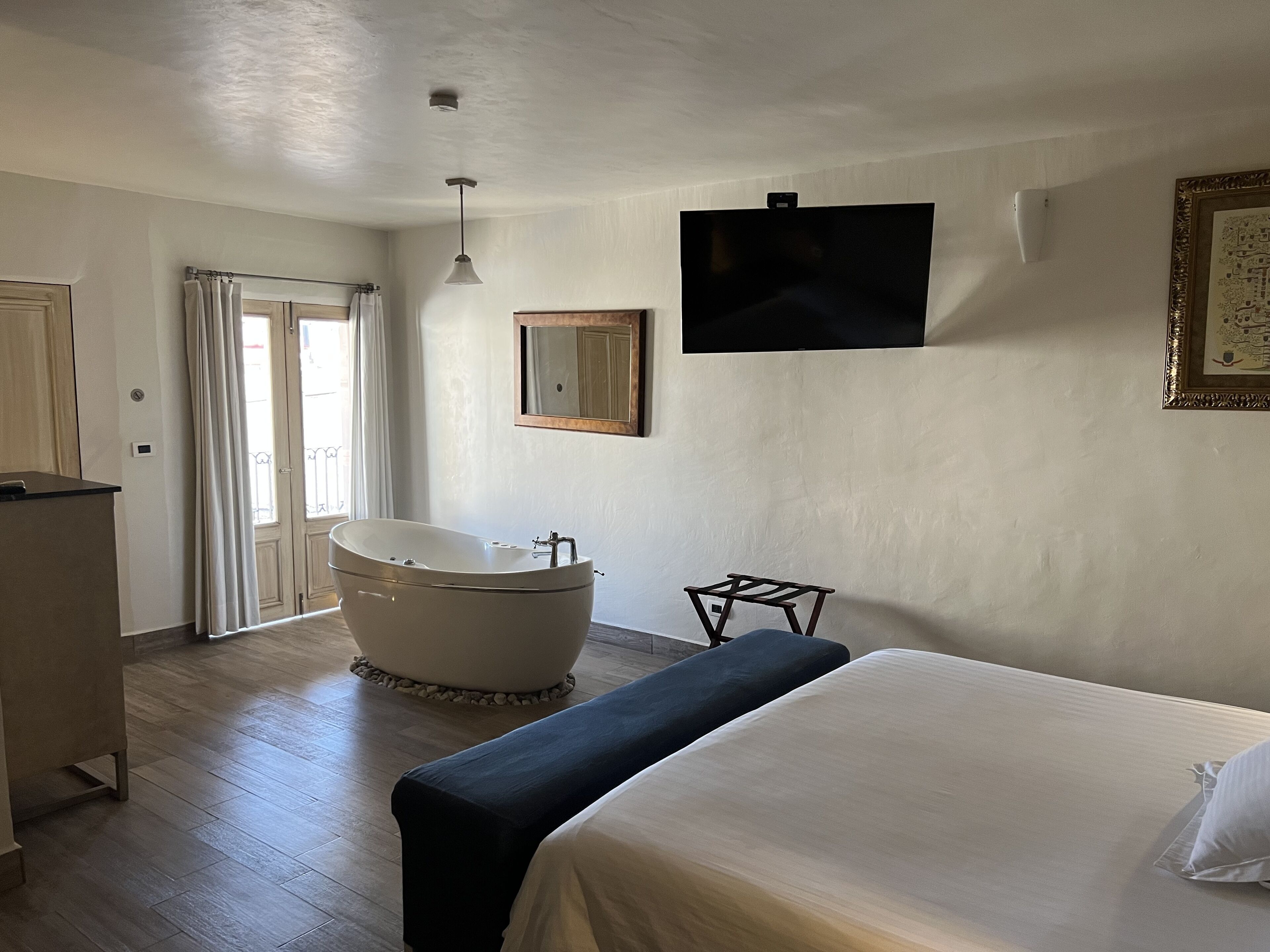 Une chambre avec un grand lit, une baignoire, une télévision et une porte donnant sur un balcon.
