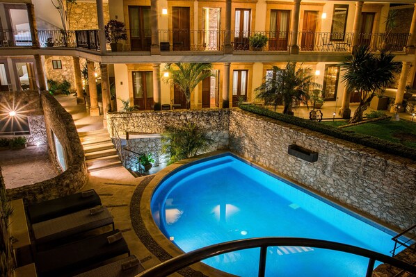 Ein mehrstöckiges Hotel mit einem zentral gelegenen Schwimmbad, Steinwänden und Balkonen mit Pflanzen.
