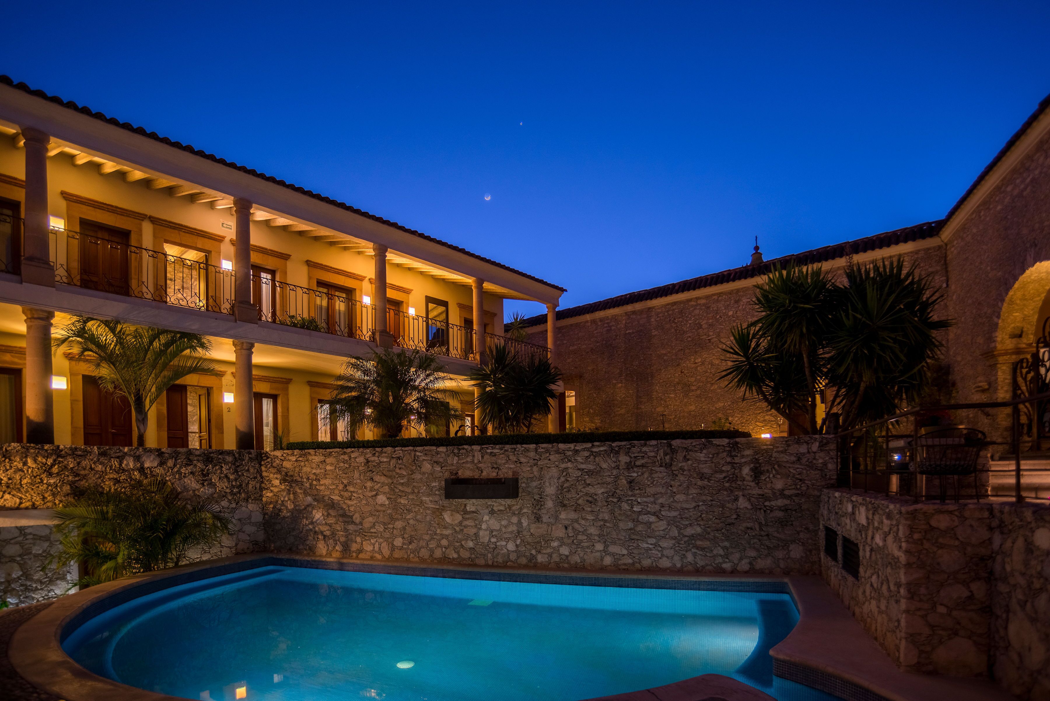 Un hotel con piscina, paredes de piedra y balcones con barandillas.