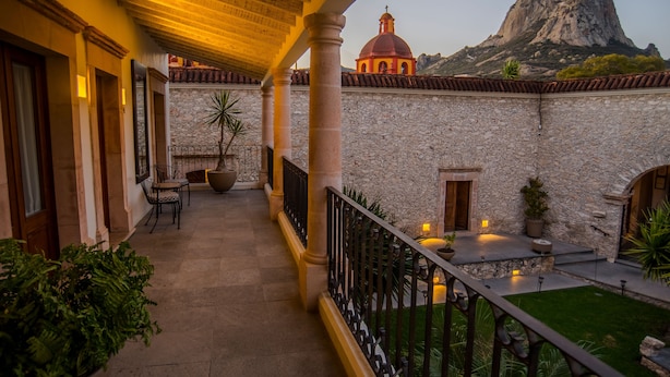 A covered balcony with stone walls, a view of a mountain, and a small building with a dome. - Hotel Boutique Casa Mateo (Ezequiel Montes)