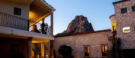 A stone building with a balcony overlooking a courtyard, a mountain in the background, and a clear sky.