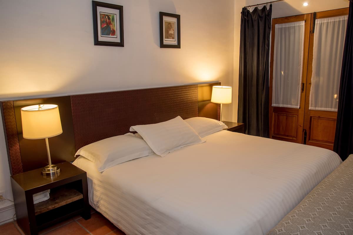 A neatly made bed with white linens, two bedside lamps, and a wooden headboard.