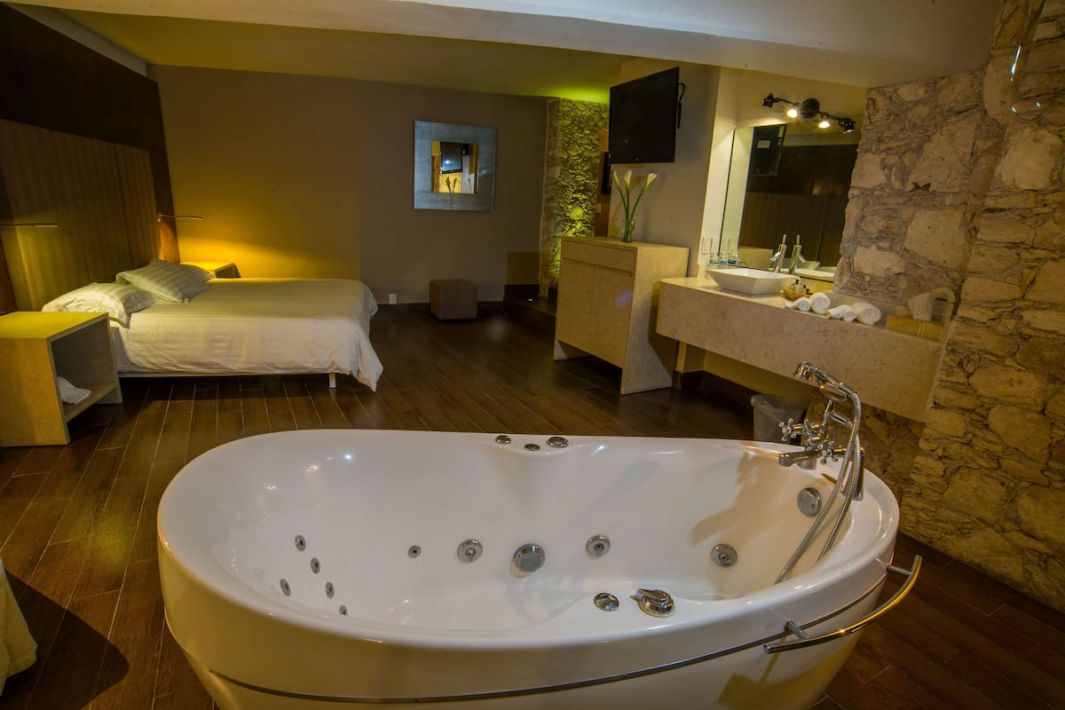 A modern bathroom with a large freestanding bathtub, a vanity with a stone accent wall, and a bed with a nightstand.