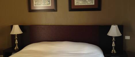 A hotel room with a large bed, two bedside tables with lamps, and two framed pictures on the wall.