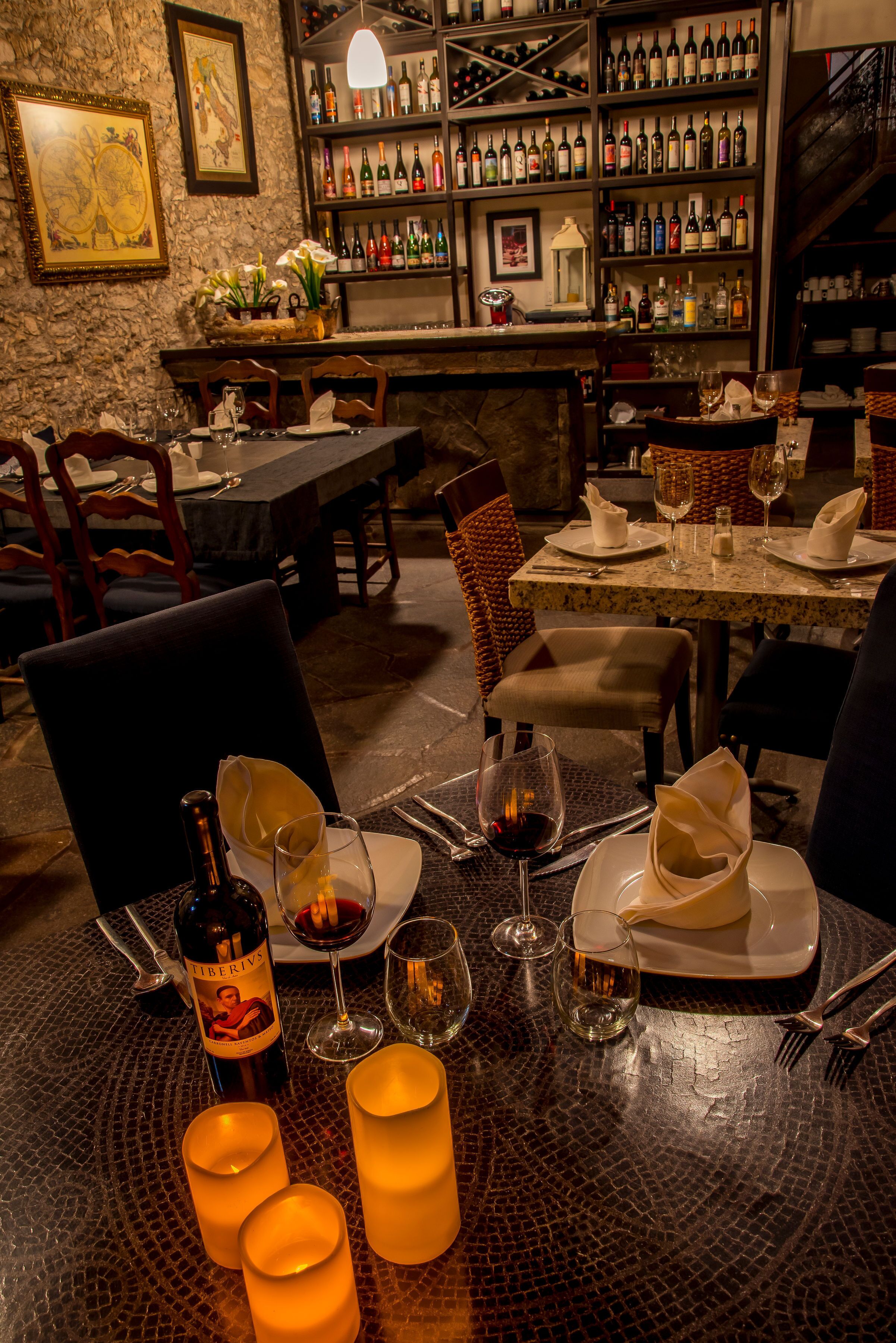 A restaurant with tables set for dining, a wine rack in the background, and a stone wall.