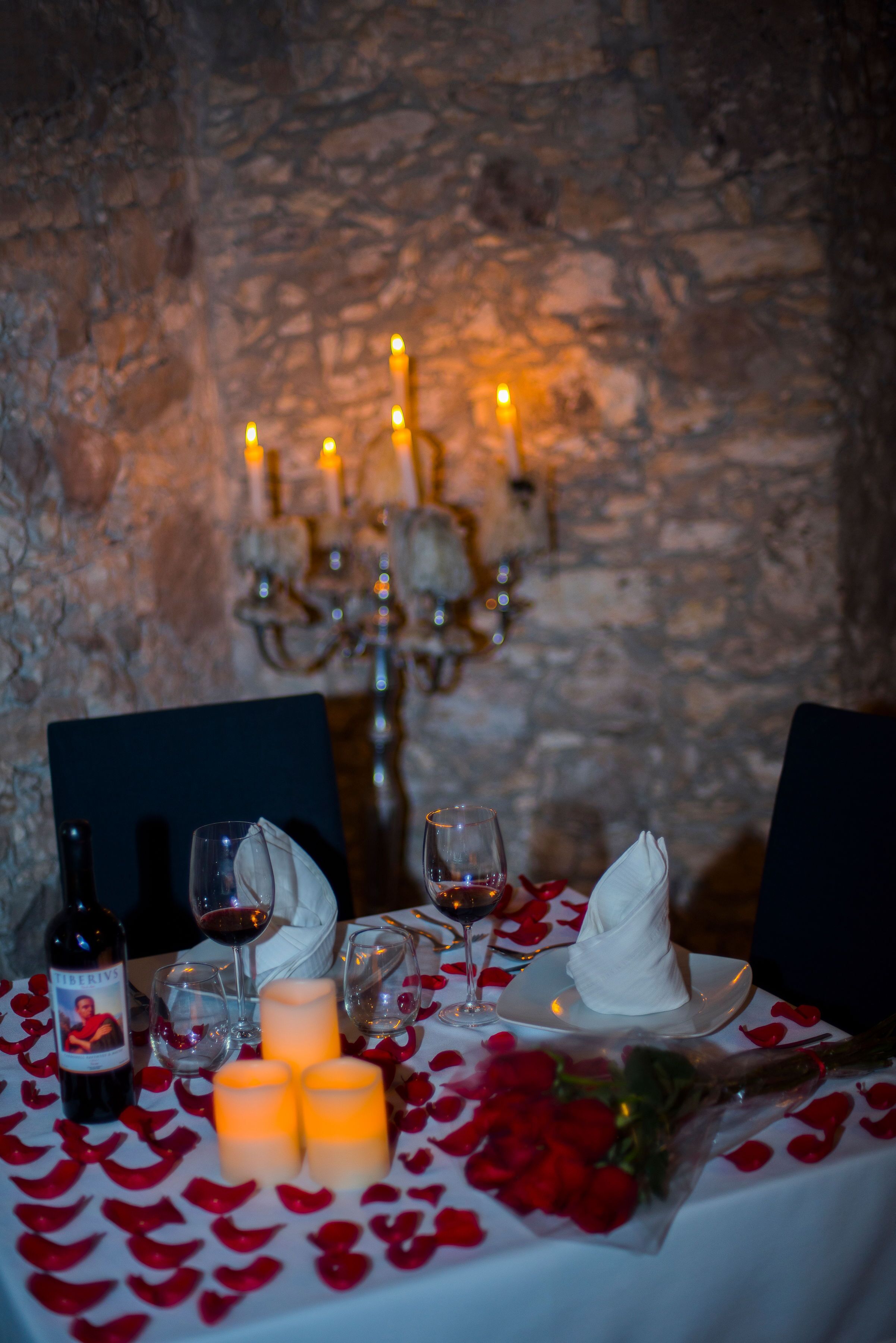 Una mesa para dos, con velas, copas de vino y pétalos de rosa.
