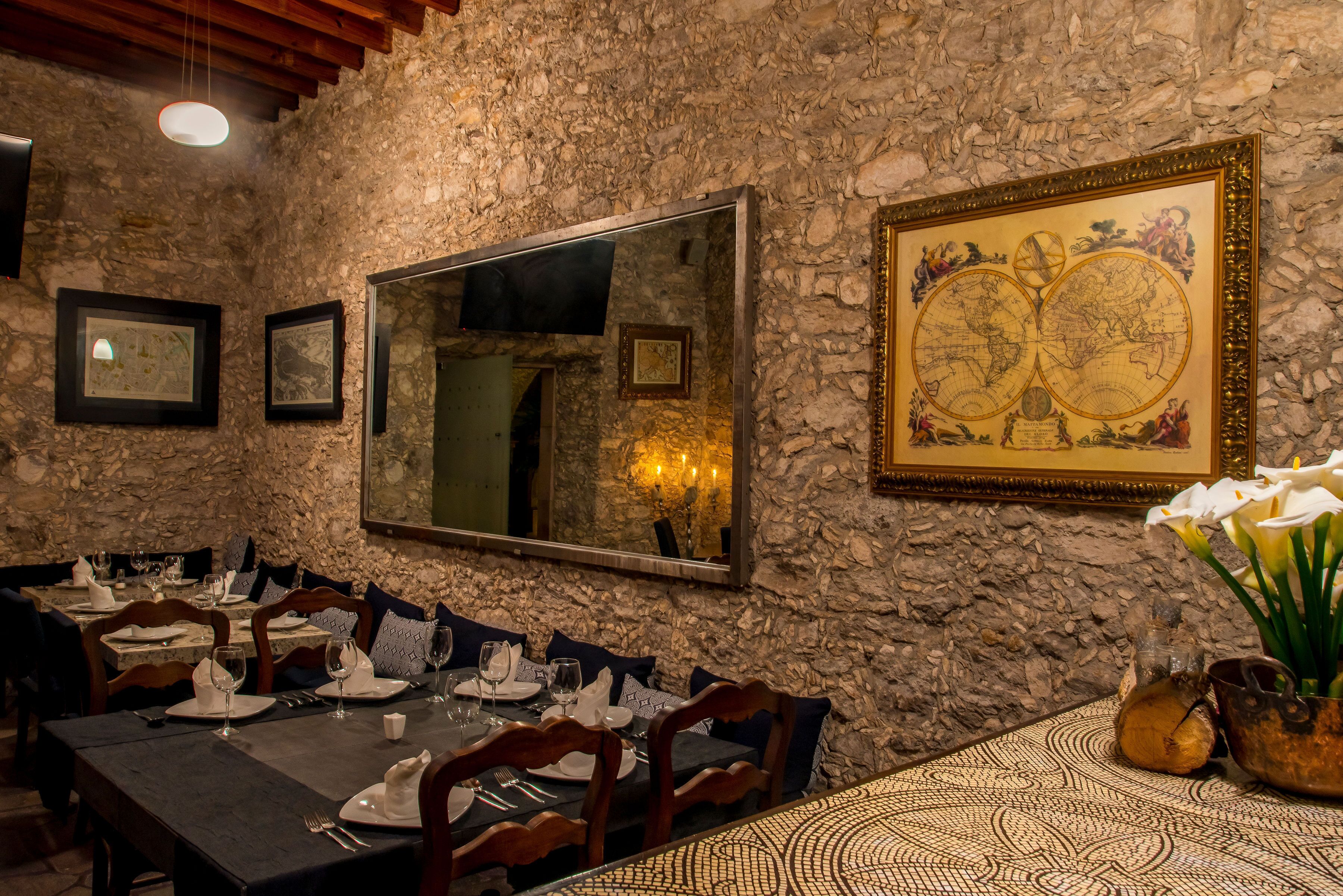 A restaurant with stone walls, a large world map, and a mirror. Tables are set with plates, glasses, and cutlery.