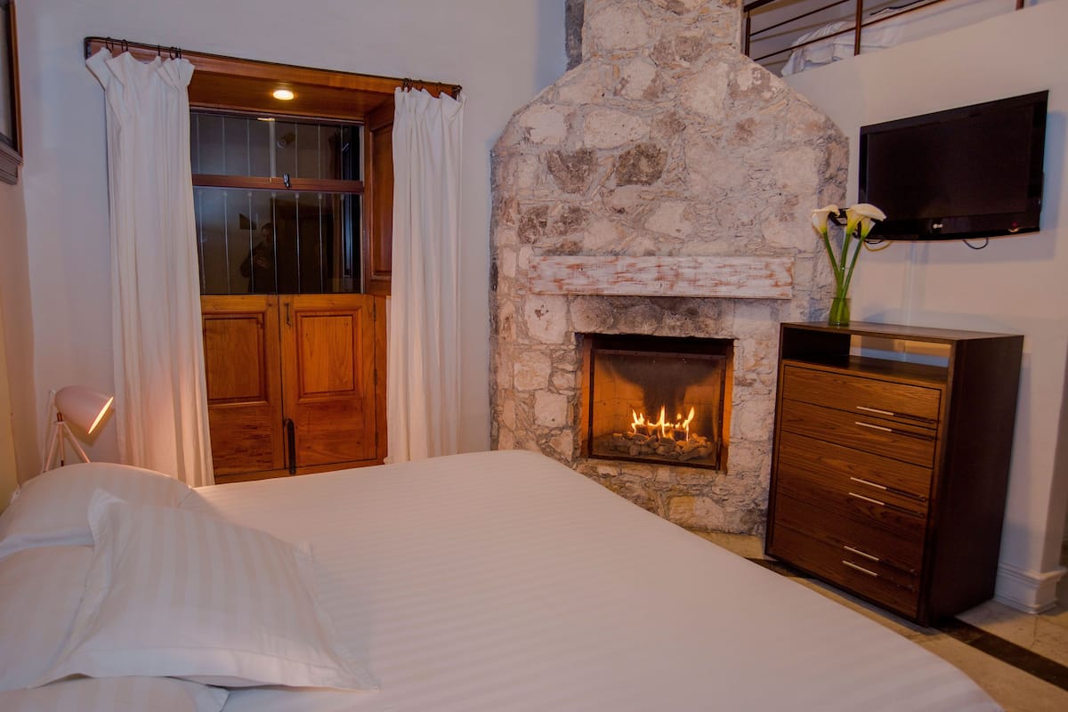 A bedroom with a stone fireplace, wooden wardrobe, and a bed with white linens.