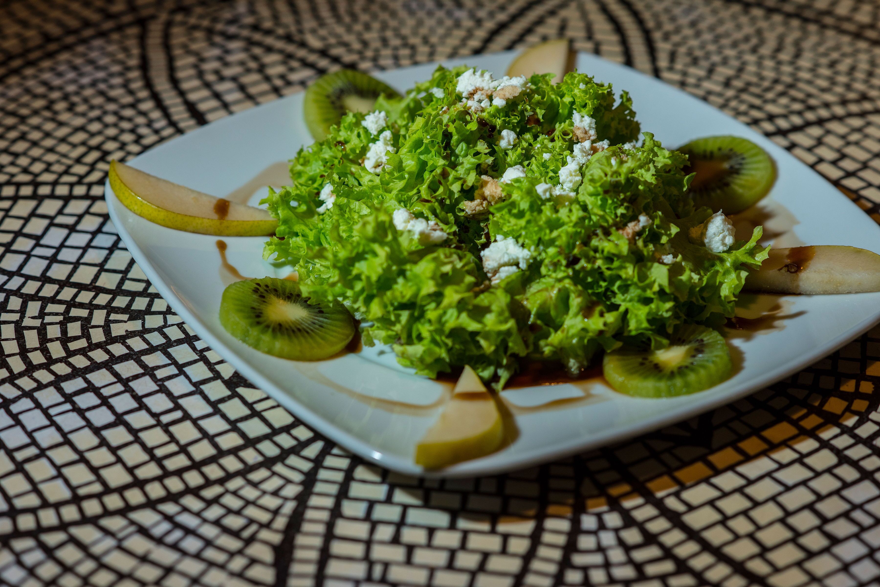 Een vierkant bord met een salade op een betegelde tafel.