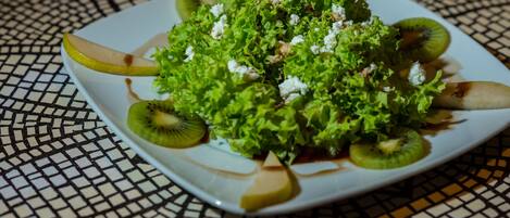 Een vierkant bord met een salade op een betegelde tafel.