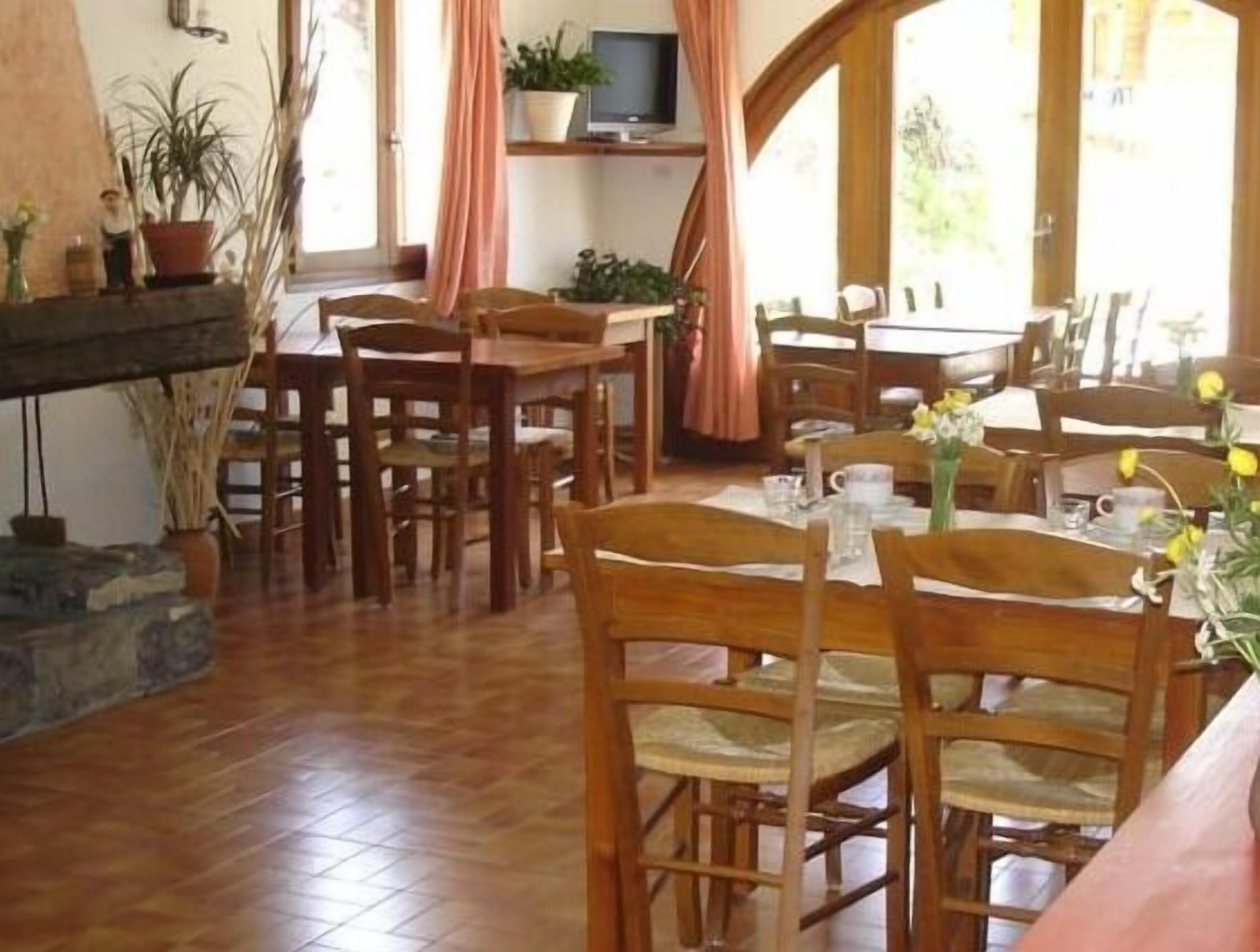A dining area with wooden tables and chairs, a stone fireplace, and potted plants.