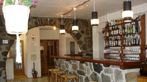 A bar area with stone walls, wooden stools, and a variety of liquor bottles. - Hôtel Le Parpaillon (Crevoux)