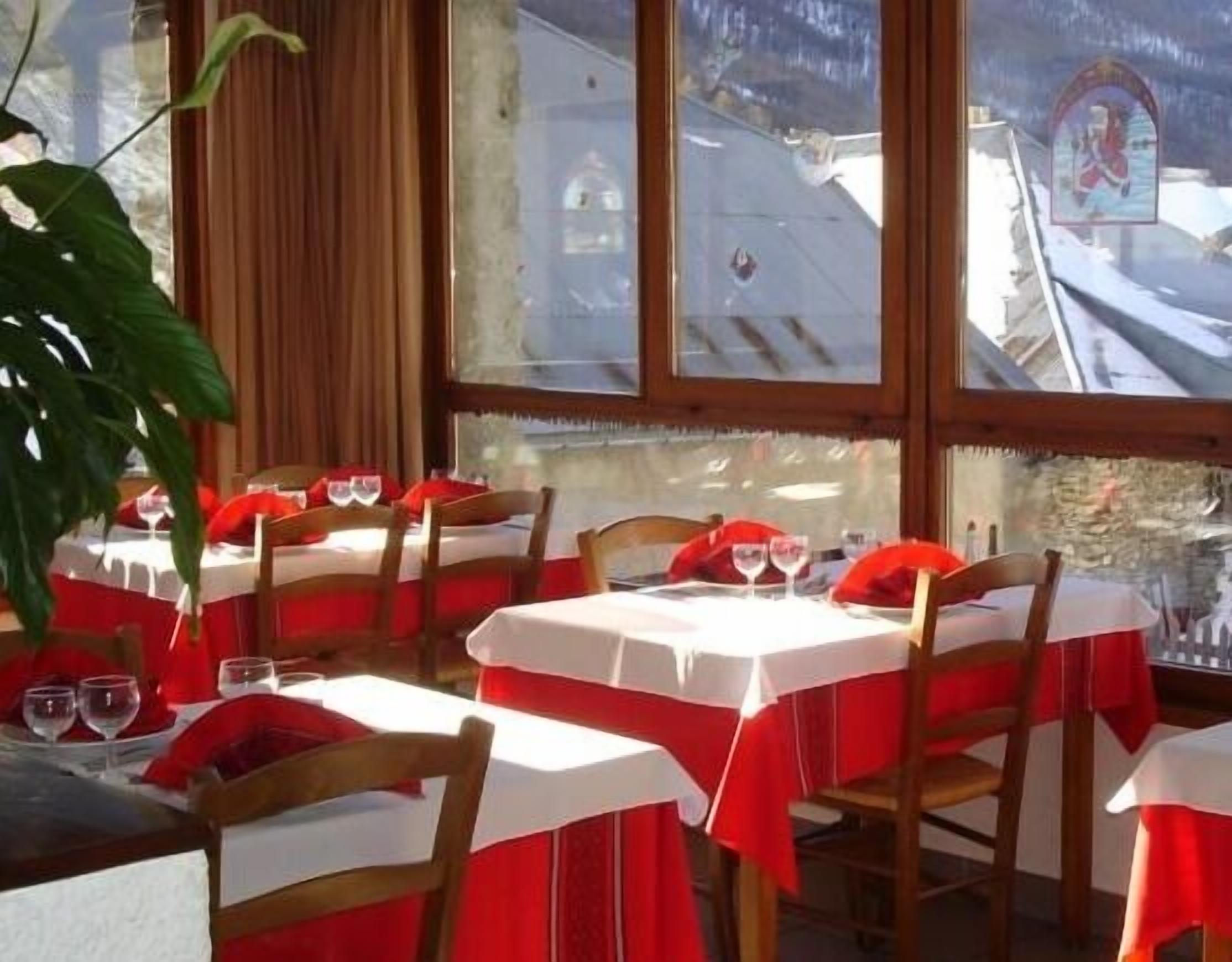 Un restaurante con varias mesas, cada una con mantel blanco y servilletas rojas.