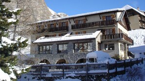 A multi-story hotel with stone walls and balconies, surrounded by snow and mountains. - Hôtel Le Parpaillon (Crevoux)