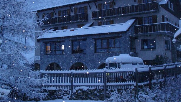 A multi-story hotel with a stone facade, balconies, and a snow-covered landscape. - Hôtel Le Parpaillon (Crevoux)