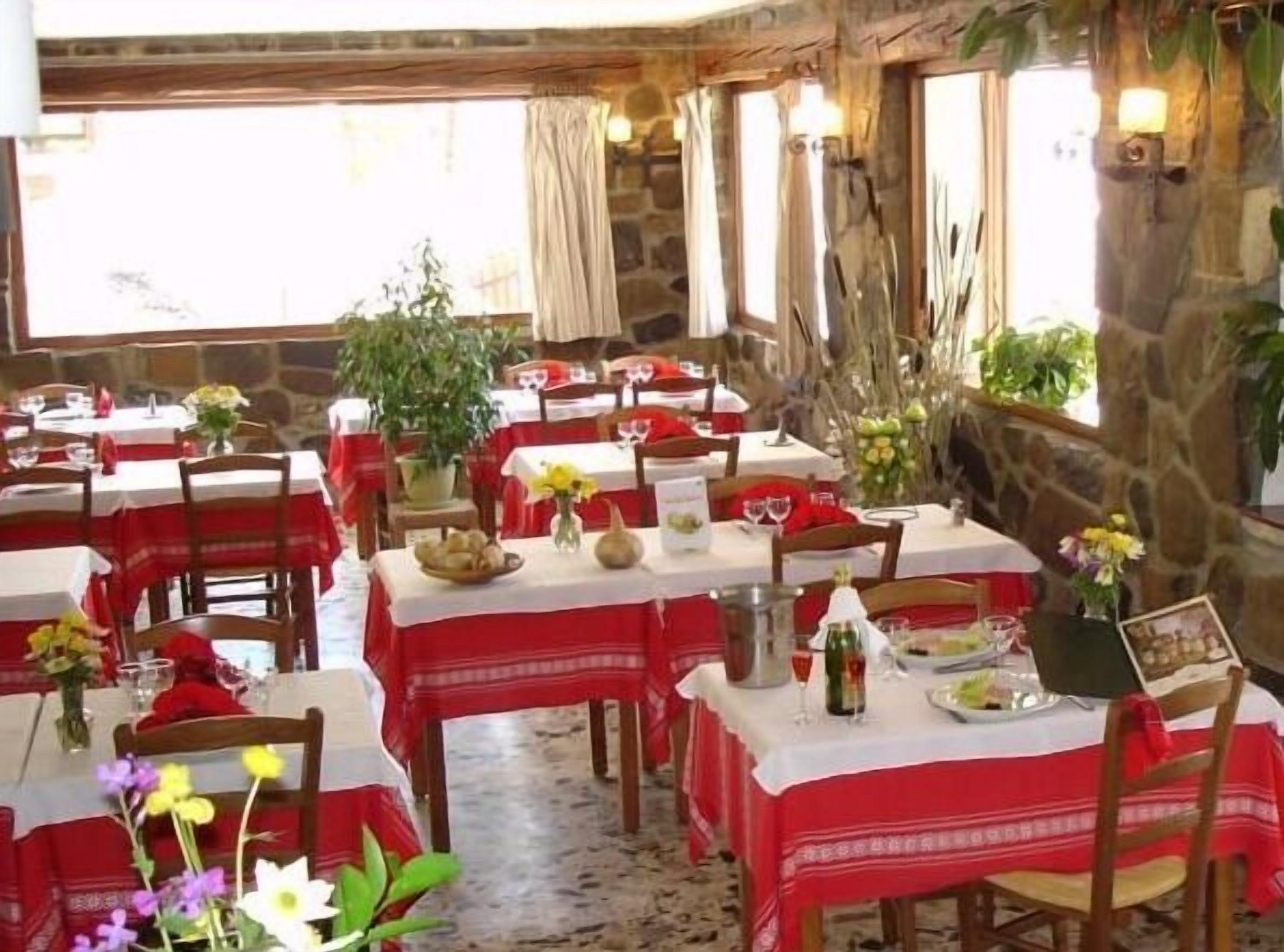 A restaurant with stone walls, red and white tablecloths, and potted plants.