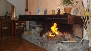 A room with a stone fireplace, a wooden table, and chairs. - Hôtel Le Parpaillon (Crevoux)