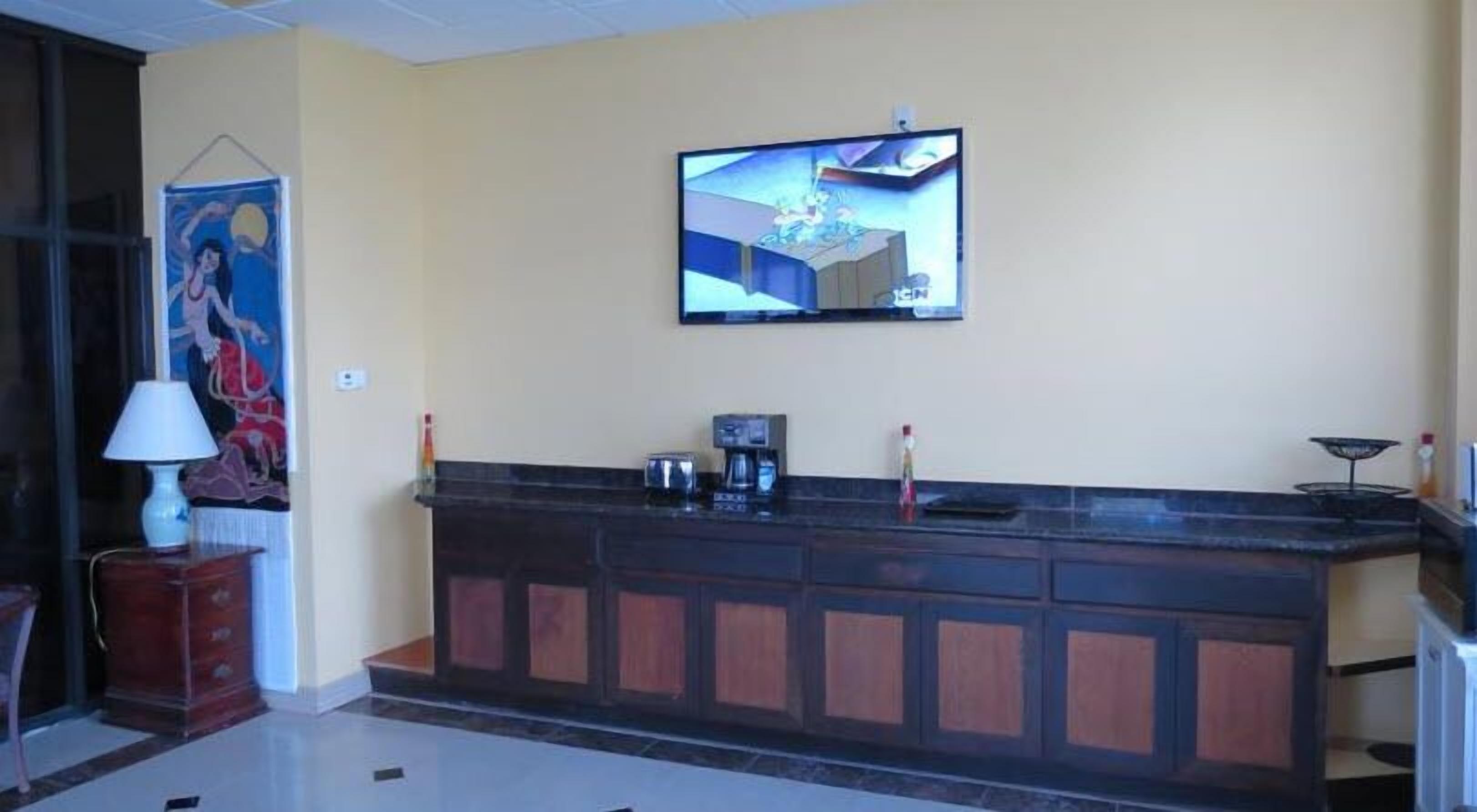A reception area with a dark wooden counter, a television mounted on the wall, and a painting on the left.