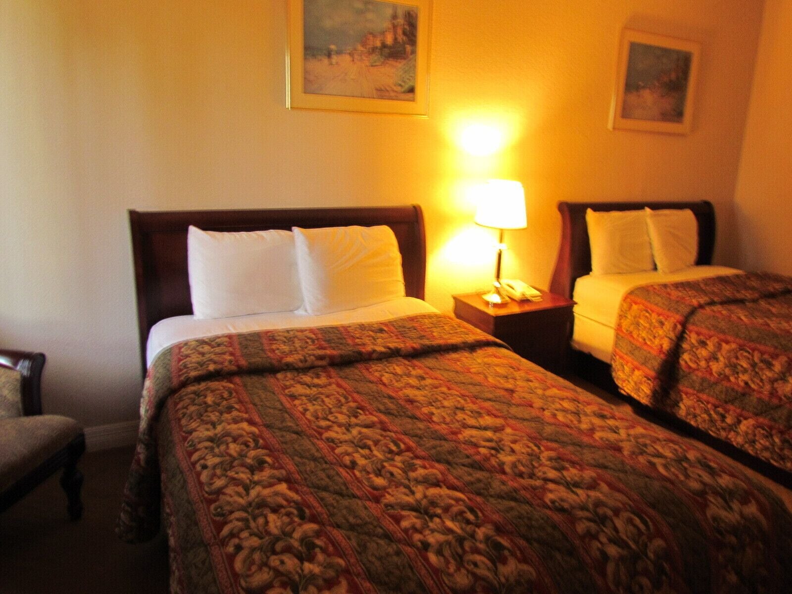 Una habitación de hotel con dos camas individuales, una mesita de noche con lámpara y una silla.
