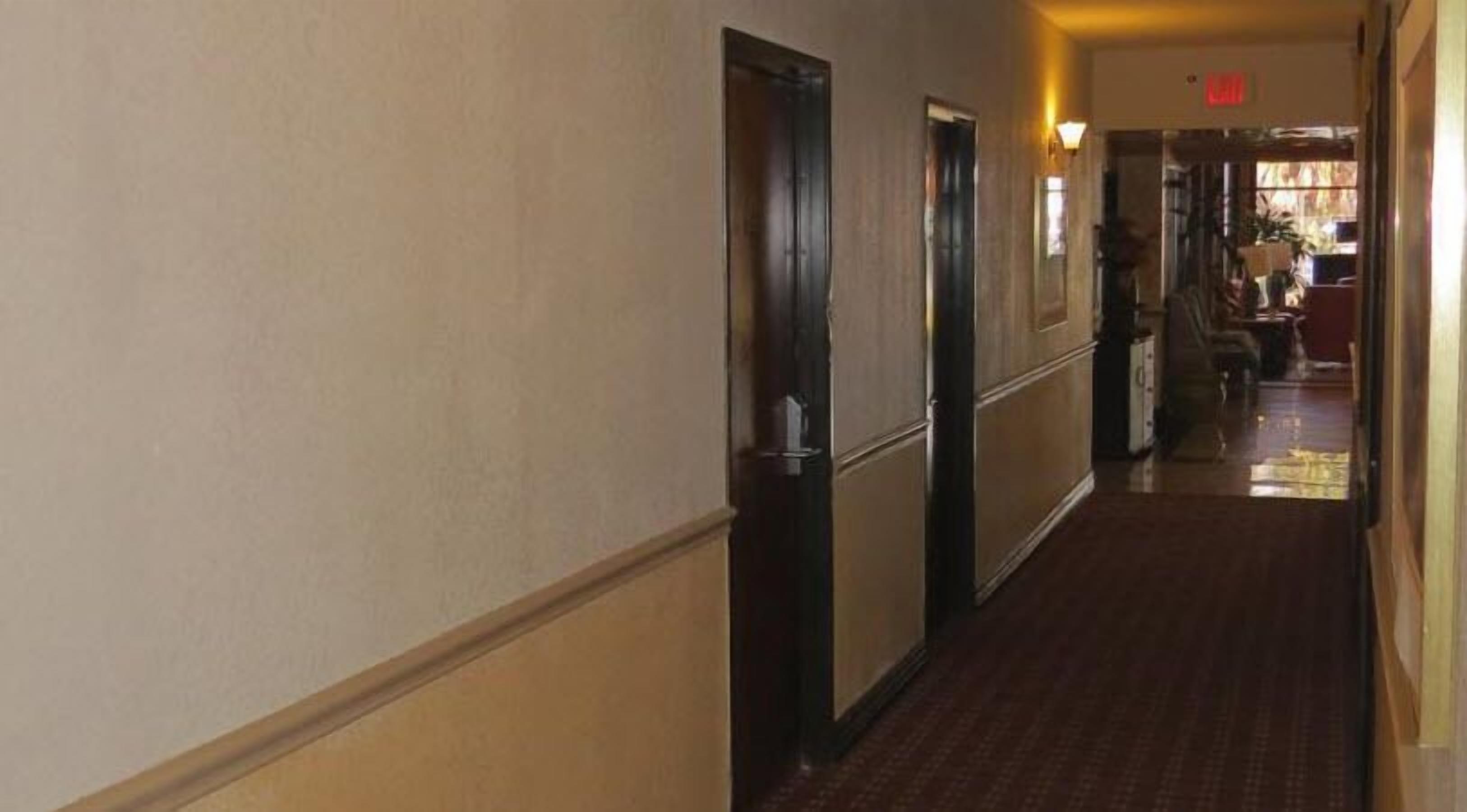 Un pasillo de hotel con puertas a la izquierda, suelo alfombrado y un vestíbulo que conduce a una habitación con ventana.