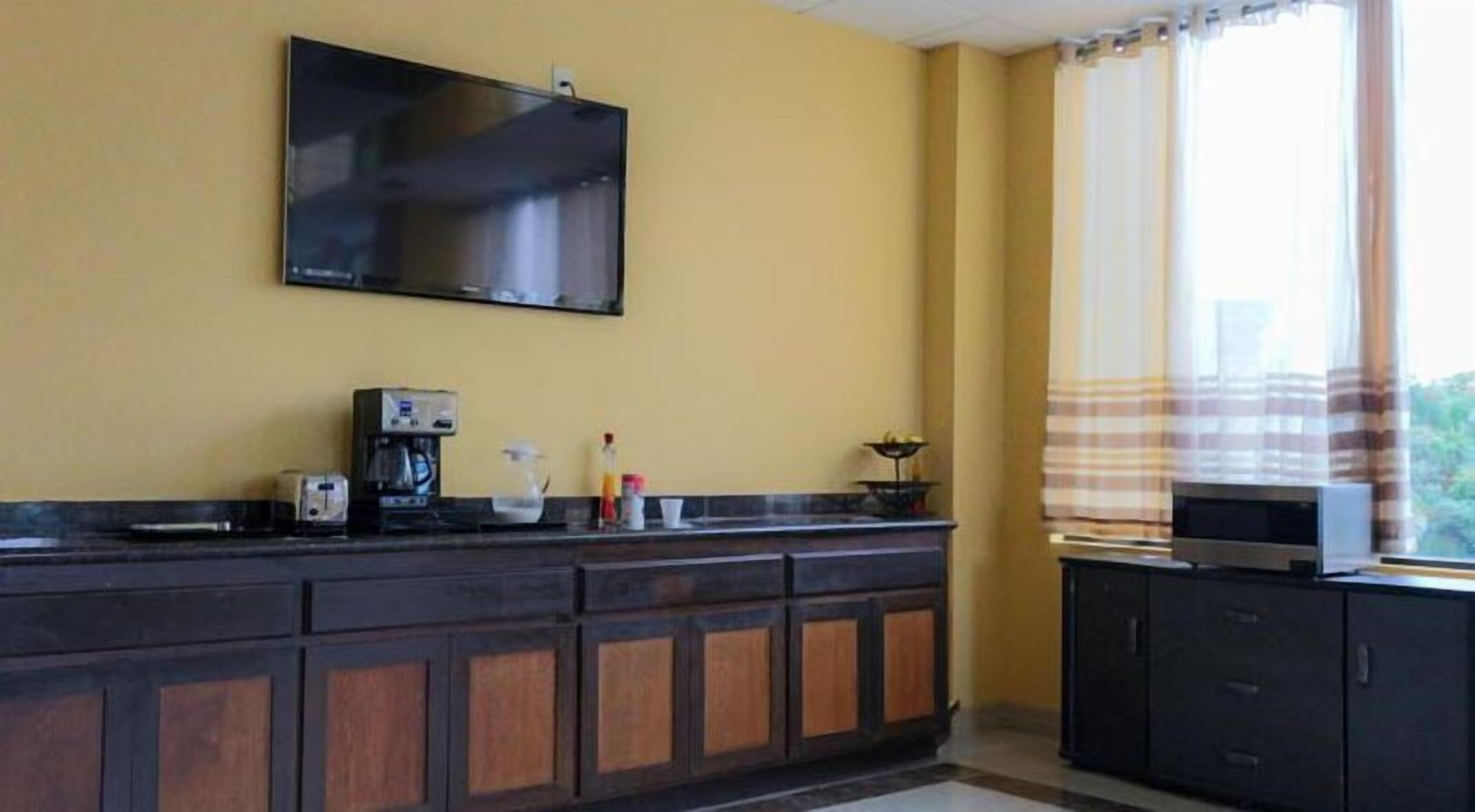 Una cocina con una televisión de pantalla plana montada en la pared, una cafetera y una ventana con cortinas.