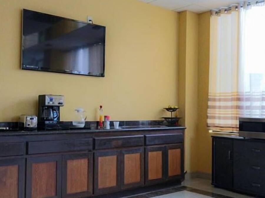 Una cocina con una televisión de pantalla plana montada en la pared, una cafetera y una ventana con cortinas.