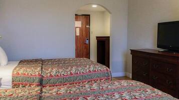 Habitación de hotel con cama, televisión, cómoda y puerta que da a otra habitación.