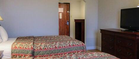Quarto de hotel com uma cama, uma televisão, cômoda e porta que dá para outro espaço.
