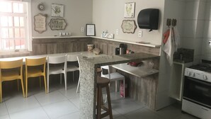 Una cocina con una isla de granito, sillas blancas, estufa y diversos utensilios de cocina.