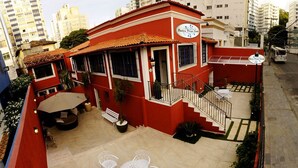 Un edificio rojo con balcón, mesas al aire libre y una escalera que conduce a la entrada.