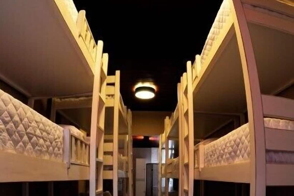 Um corredor com beliches dispostos em ambos os lados, piso de madeira e escada central.