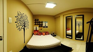 Un dormitorio con cama, un adhesivo de árbol en la pared, un espejo y una estantería con objetos decorativos.