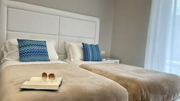 Une chambre d’hôtel avec deux lits, une tête de lit blanche et une table de chevet avec une lampe.