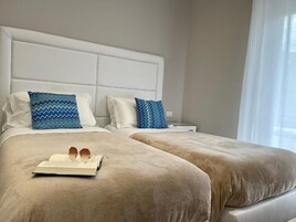 A hotel room with two beds, a white headboard, and a bedside table with a lamp.