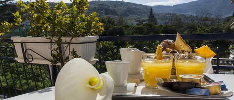 A breakfast tray with orange juice, toast, and a white flower on a balcony with a mountain view.