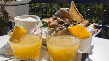 Une table dressée pour le petit-déjeuner, avec deux verres de jus d’orange, une tasse de café et une variété de viennoiseries.