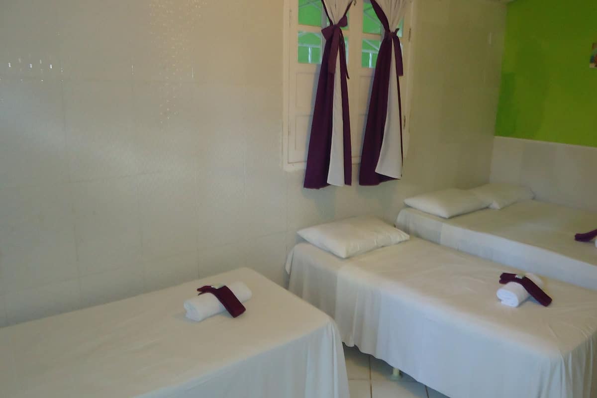 Ein Hotelzimmer mit drei Einzelbetten, jeweils mit weißer Bettdecke und einem zusammengerollten Handtuch mit roter Schleife.