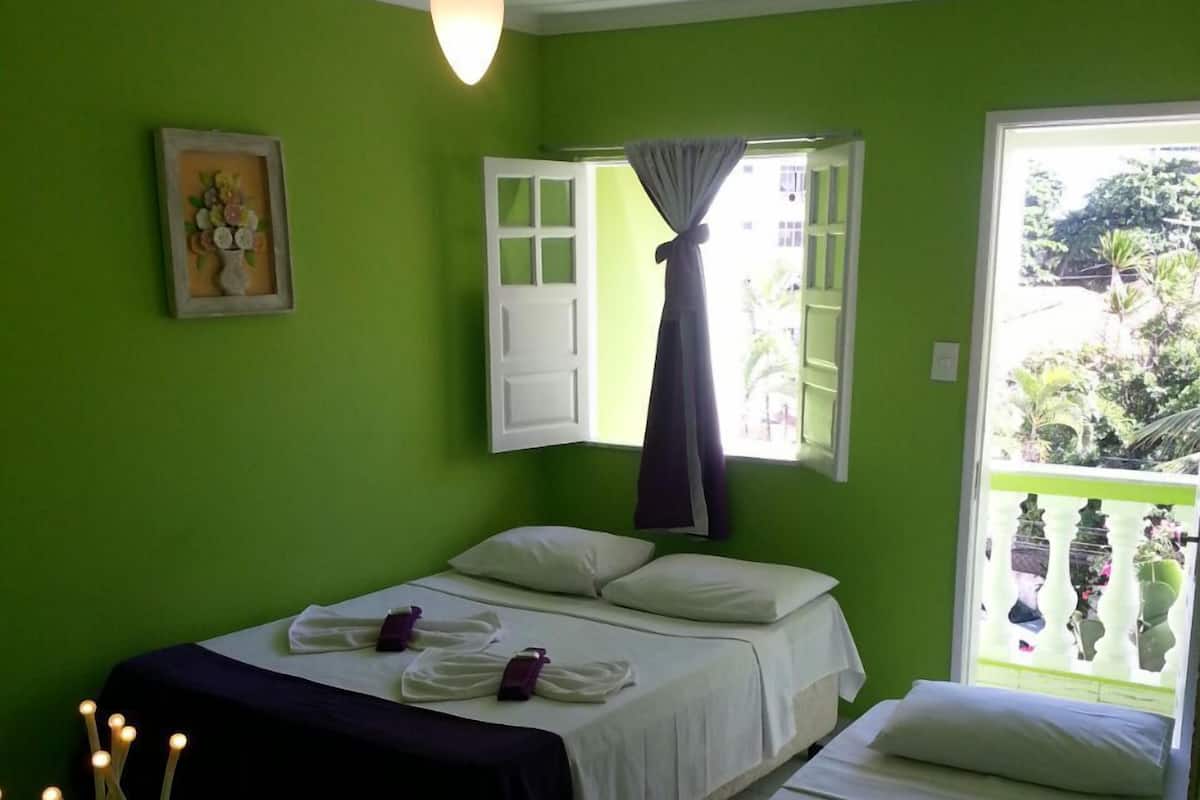 Ein Zimmer mit zwei Betten, einem Deckenventilator, einem Fenster mit Vorhängen und einem gerahmten Bild an der Wand.