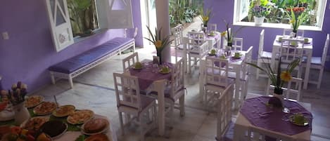 A dining area with white tables and purple walls, featuring a variety of dishes and a ceiling fan.