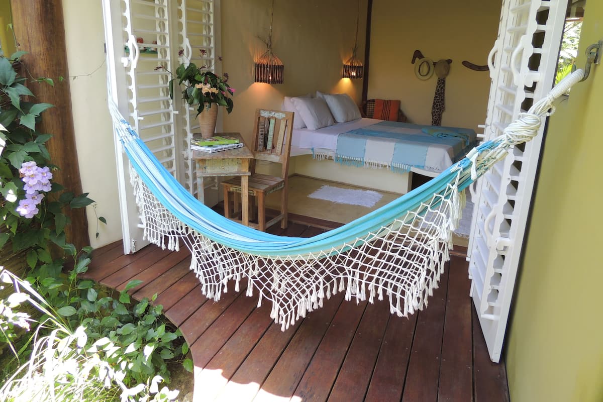 A hammock on a wooden deck with a bed and a chair in the background.