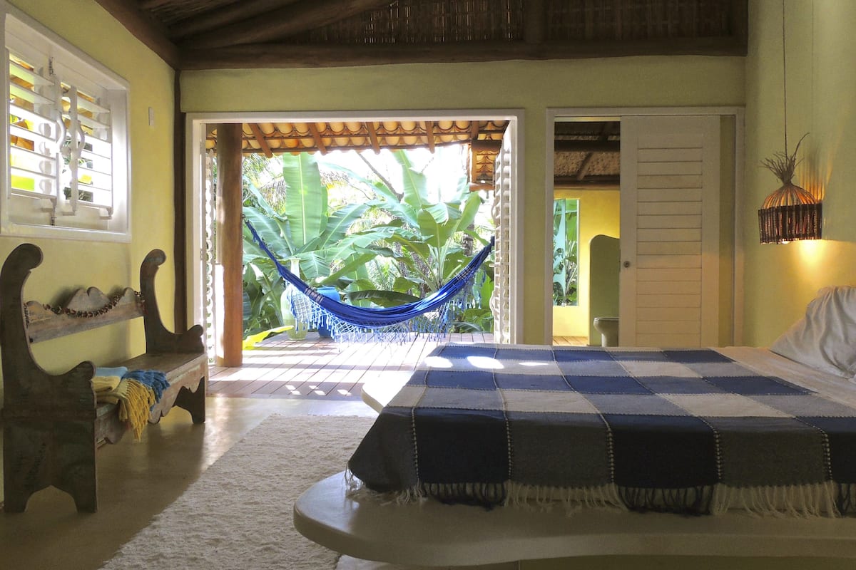 A bedroom with a bed, a hammock, a bench, and a view of a garden.
