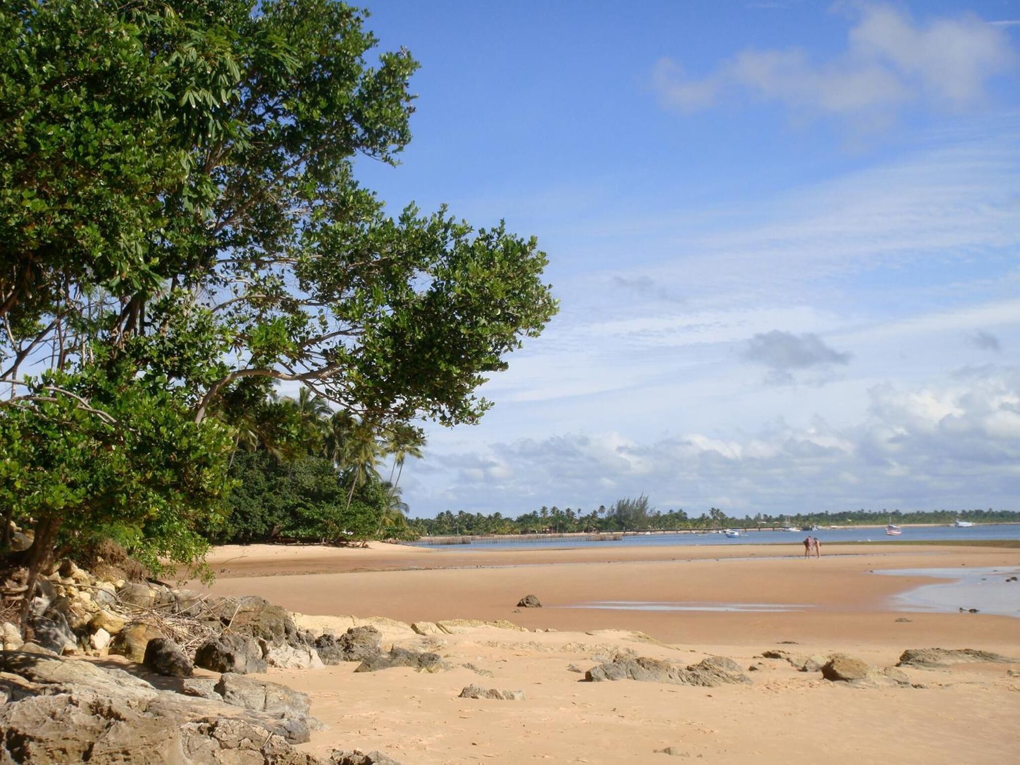 Ein Strand mit felsigem Vordergrund, Sandstrand und blauem Himmel.