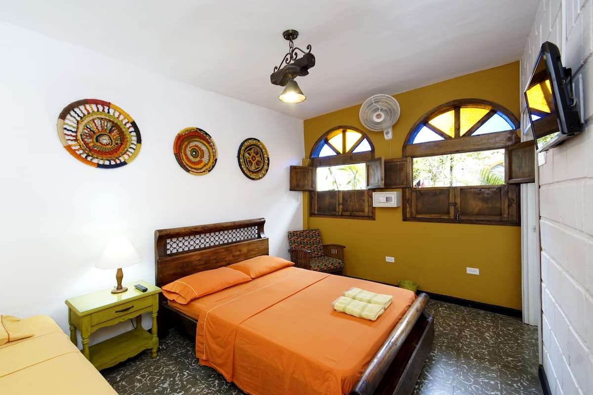 A bedroom with a bed, a nightstand, a chair, a fan, and decorative plates on the wall.