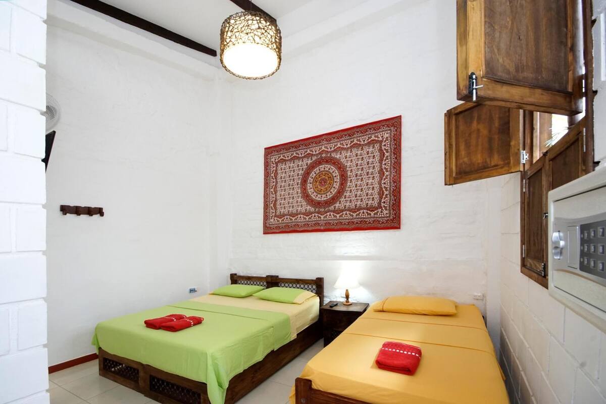 A room with two beds, a tapestry, a wooden cabinet, and a ceiling light fixture.