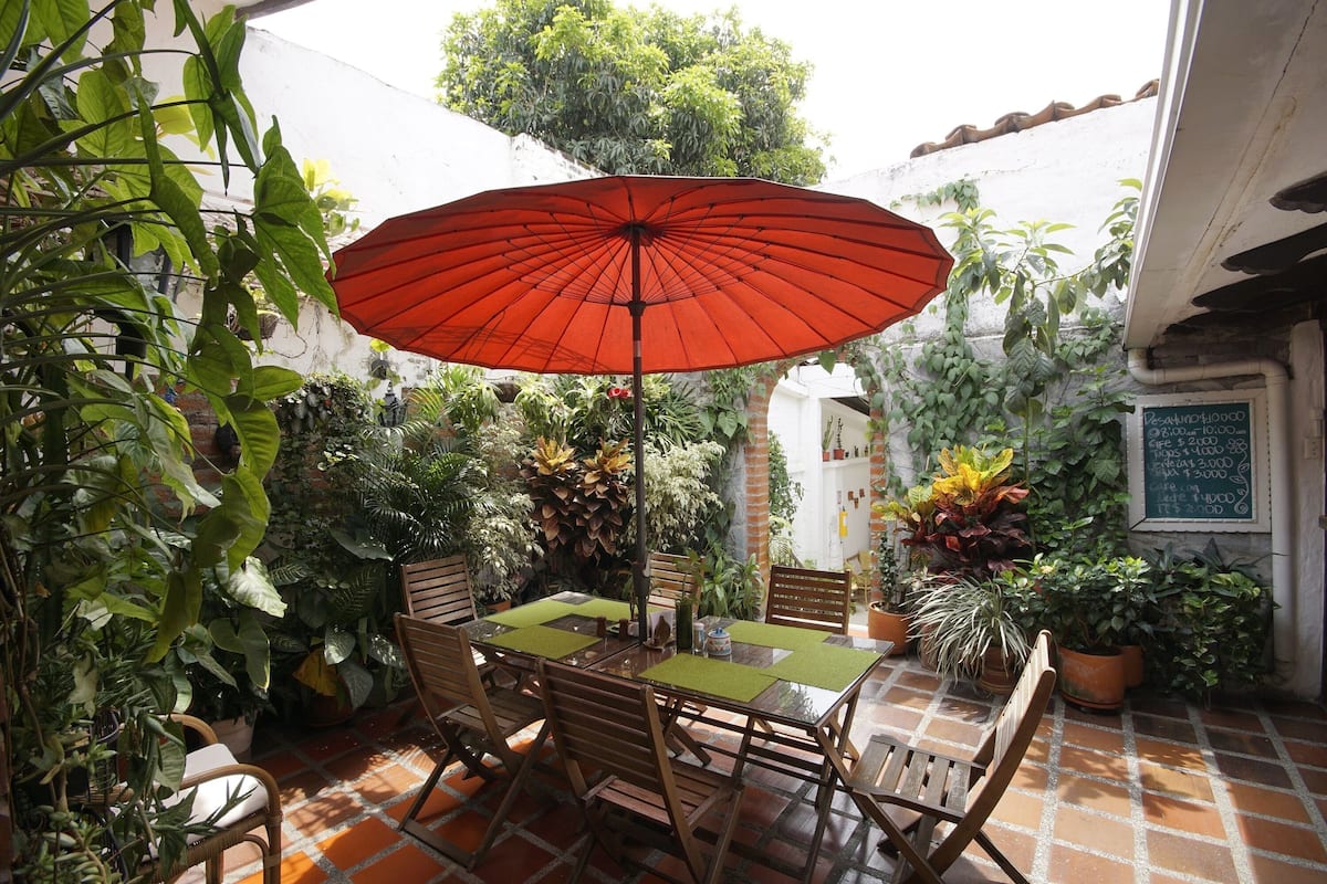 An outdoor patio with a red umbrella, wooden chairs, and a table.