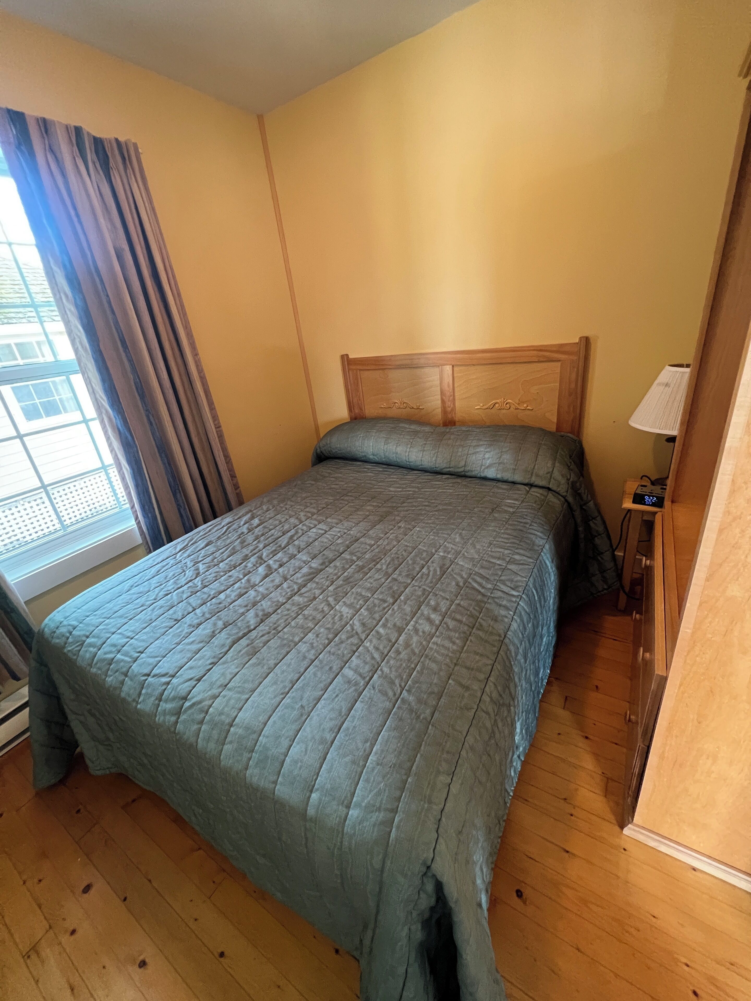 Une chambre  à coucher avec un lit en bois, une table de chevet avec une lampe et une fenêtre avec des rideaux.