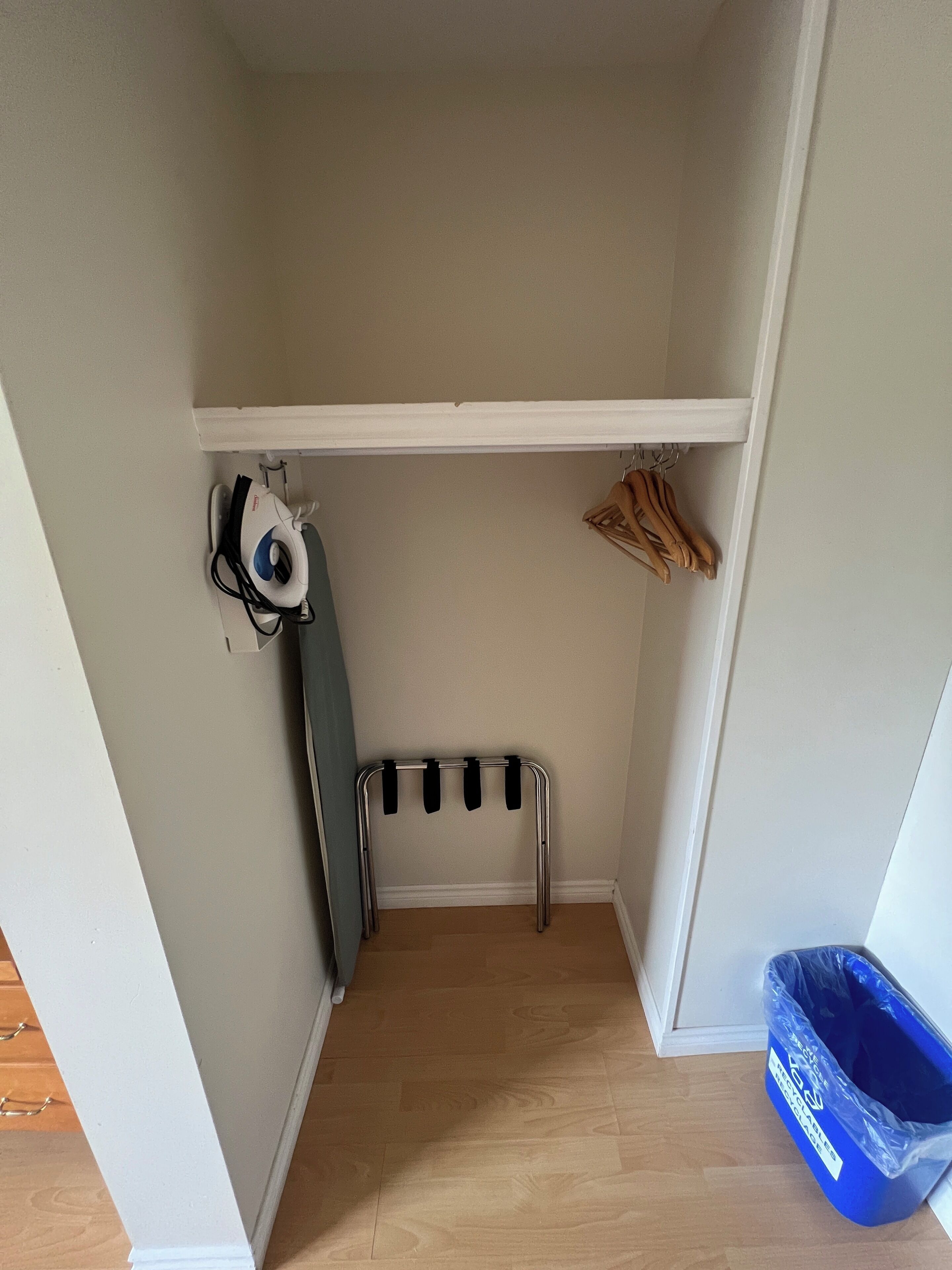 A small, narrow room with a wooden floor, a white wall, and a shelf with hanging clothes.