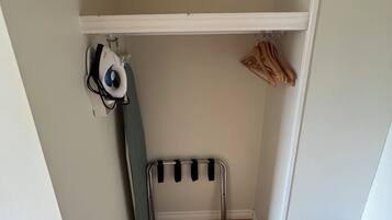 A small, narrow room with a wooden floor, a white wall, and a shelf with hanging clothes.