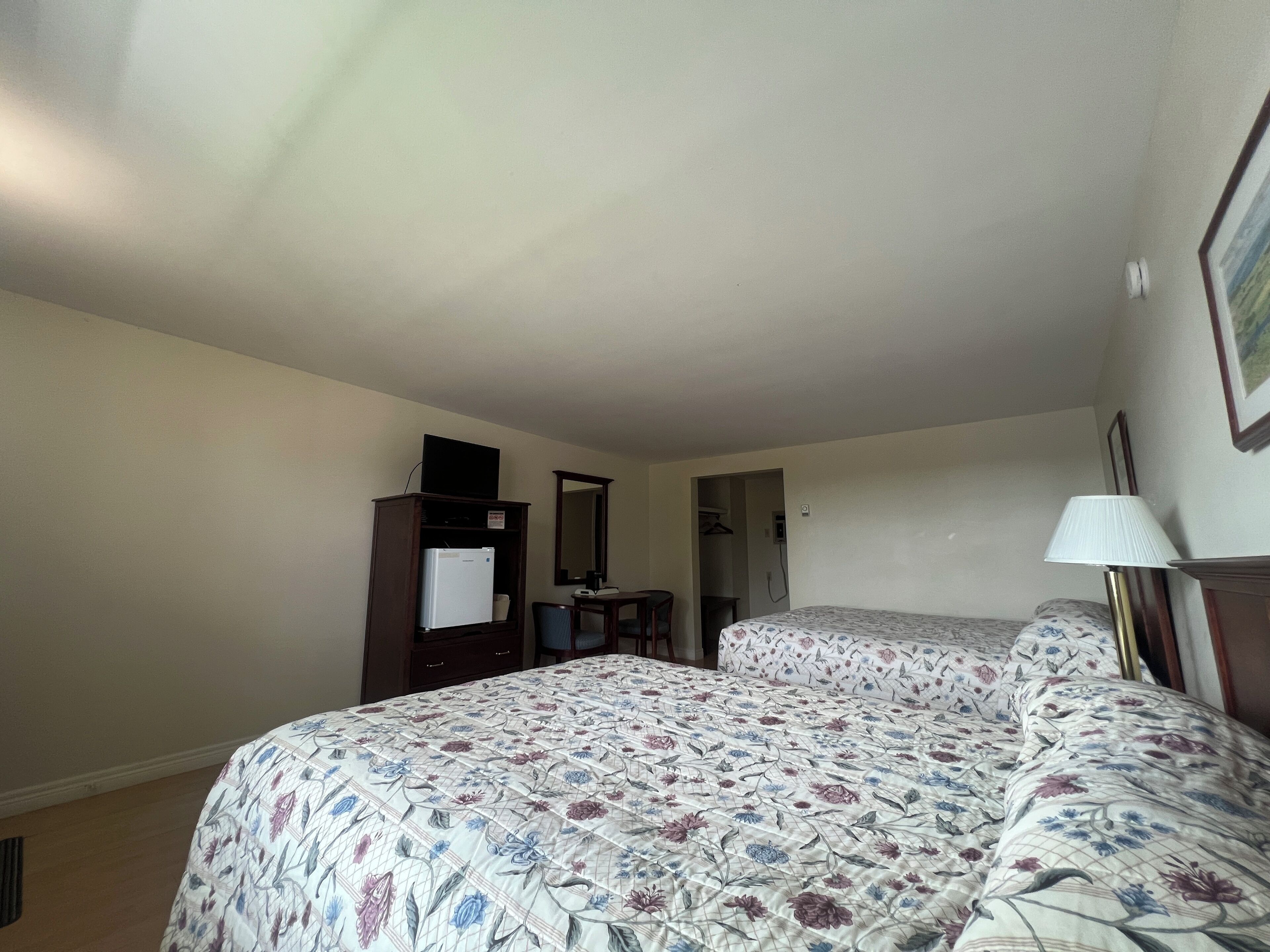 A hotel room with two beds, a desk, a wardrobe, and a mirror.